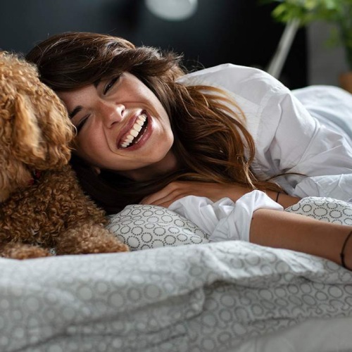 lifestyle image of a woman and dog on a bright bed