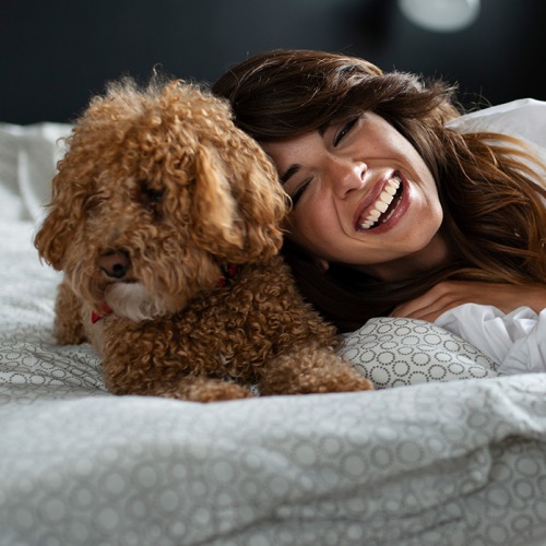 lifestyle image of a woman and dog on a bright bed